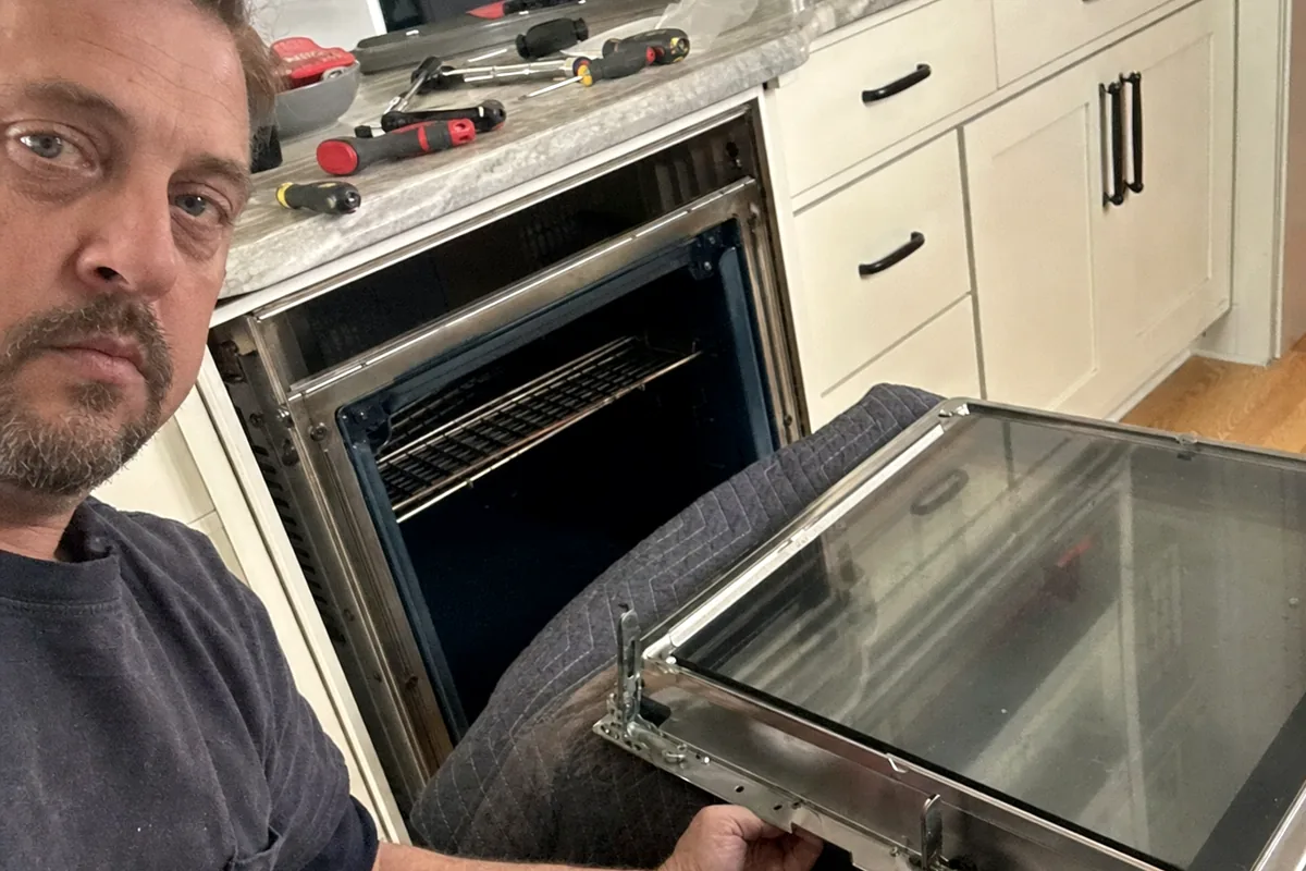 An oven door laid flat on its hinges with the inner glass panel drawn out of the frame, kitchen counter behind