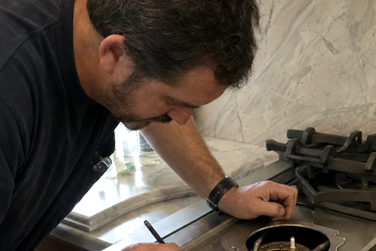 A burner head lifted clear of a gas range so the port ring and the igniter underneath can be inspected
