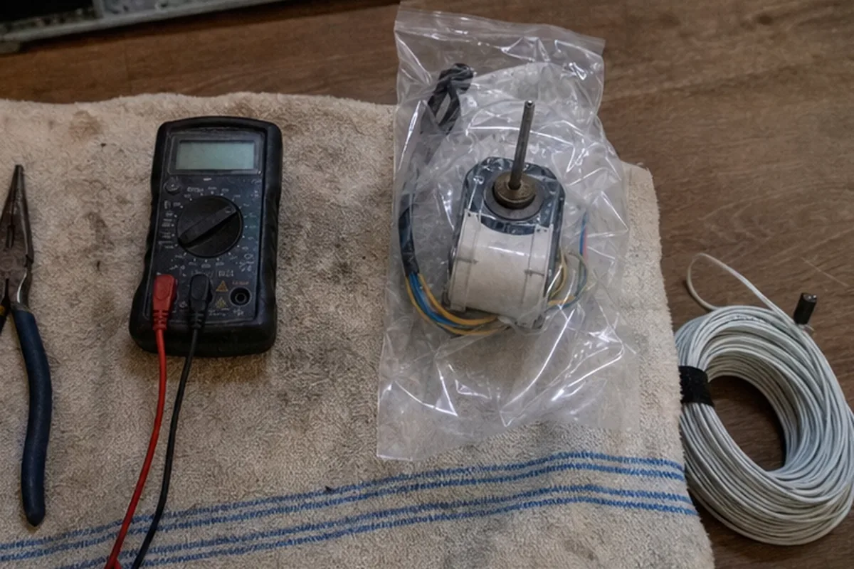 A digital multimeter with its probes laid out on a drop cloth beside a bagged replacement motor, ready for electrical testing